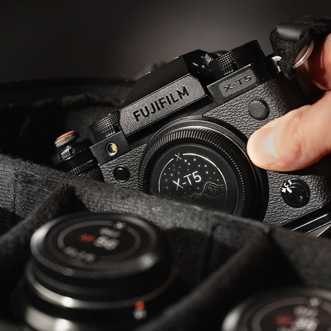 Fujifilm X-T5 with a stealth label resting in a padded camera bag, a hand reaching for it