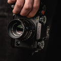 Fujifilm camera held in one hand against a dark background, stealth label on the viewfinder housing