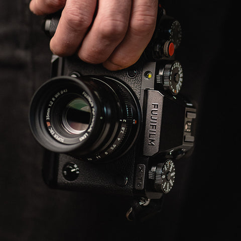 Fujifilm camera held in one hand against a dark background, stealth label on the viewfinder housing